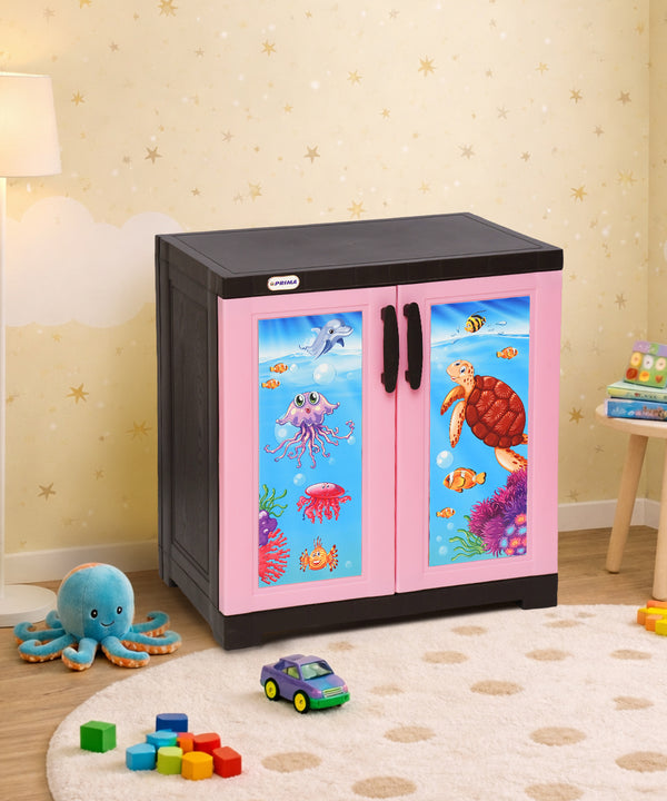 A children's storage cabinet with a black top and base, and pink double doors featuring colorful underwater sea life illustrations, shown in a decorated playroom setting.