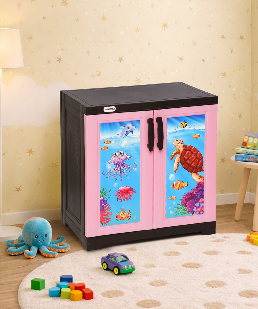 A children's storage cabinet with a black top and base, and pink double doors featuring colorful underwater sea life illustrations, shown in a decorated playroom setting.